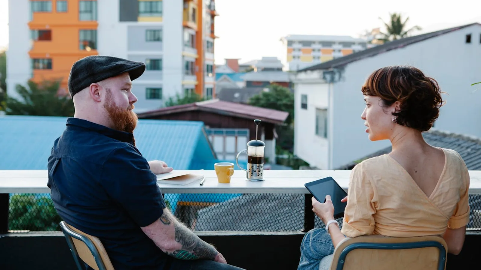 A man and a woman talking at a cafe table on a sunny rooftop terrace