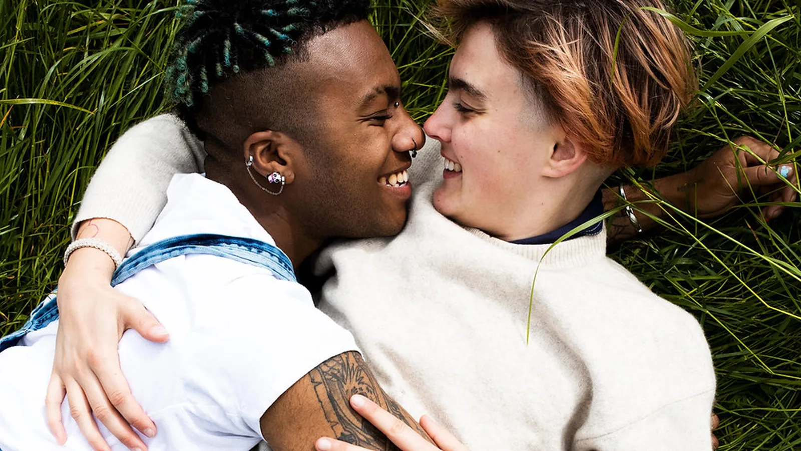 Two smiling people embracing nose to nose while lying in long grass