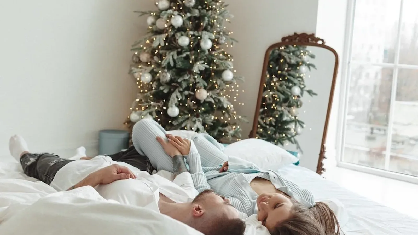 A couple lying on a white bed and talking, a Christmas tree in the background