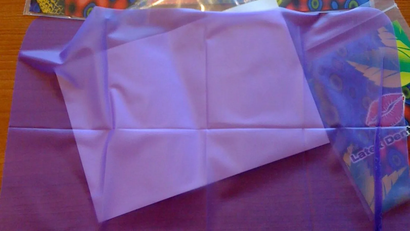 A translucent purple latex dental dam laid flat on a wooden table beside its colorful fruit-printed retail packaging