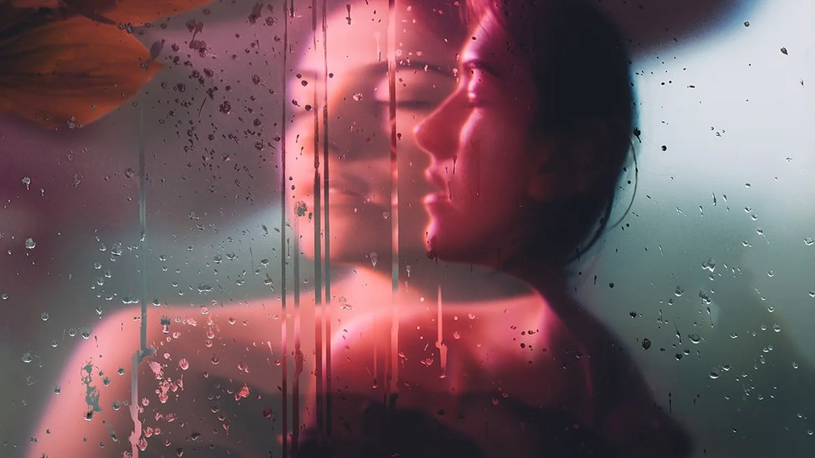 A woman's face seen through a rain-streaked window in pink light