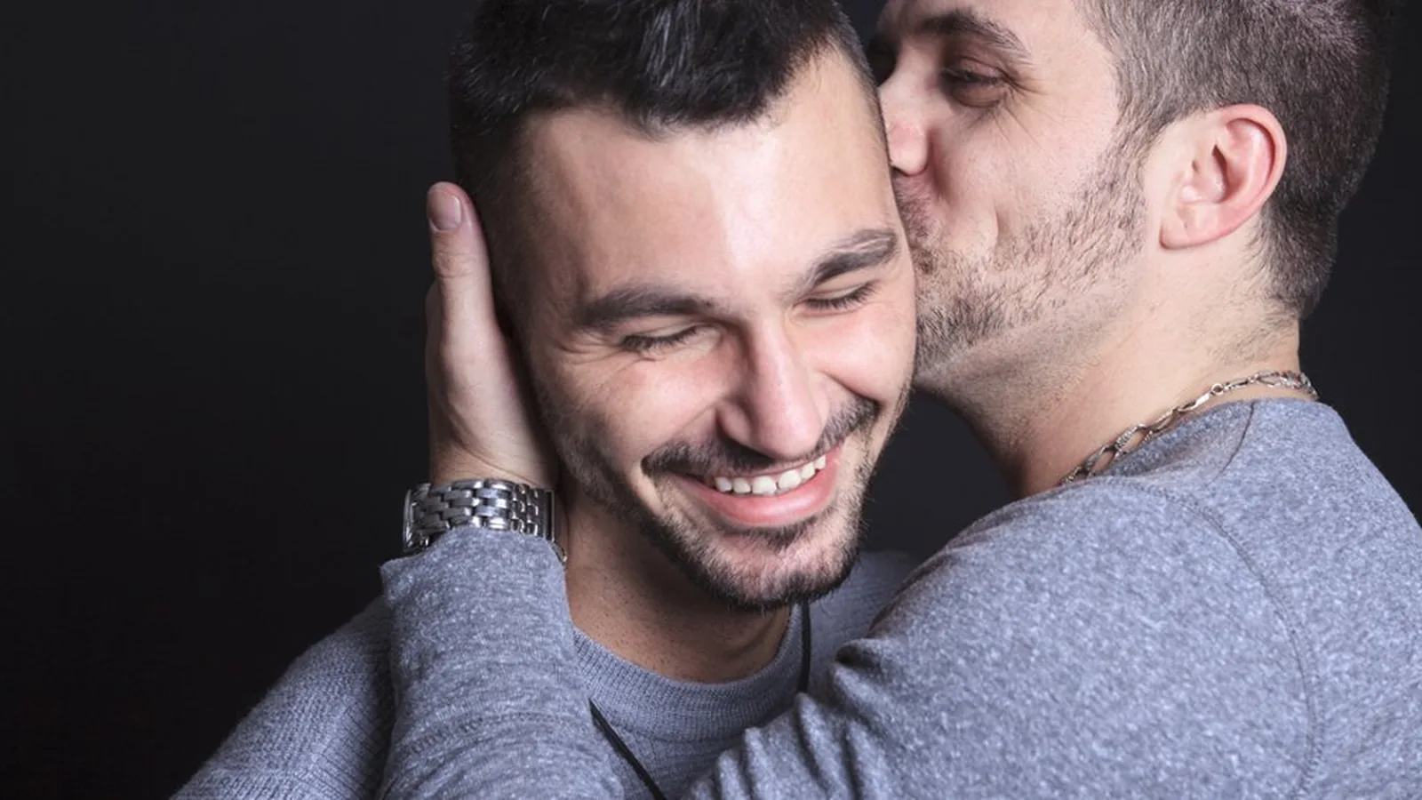 A smiling man being kissed on the cheek by his male partner