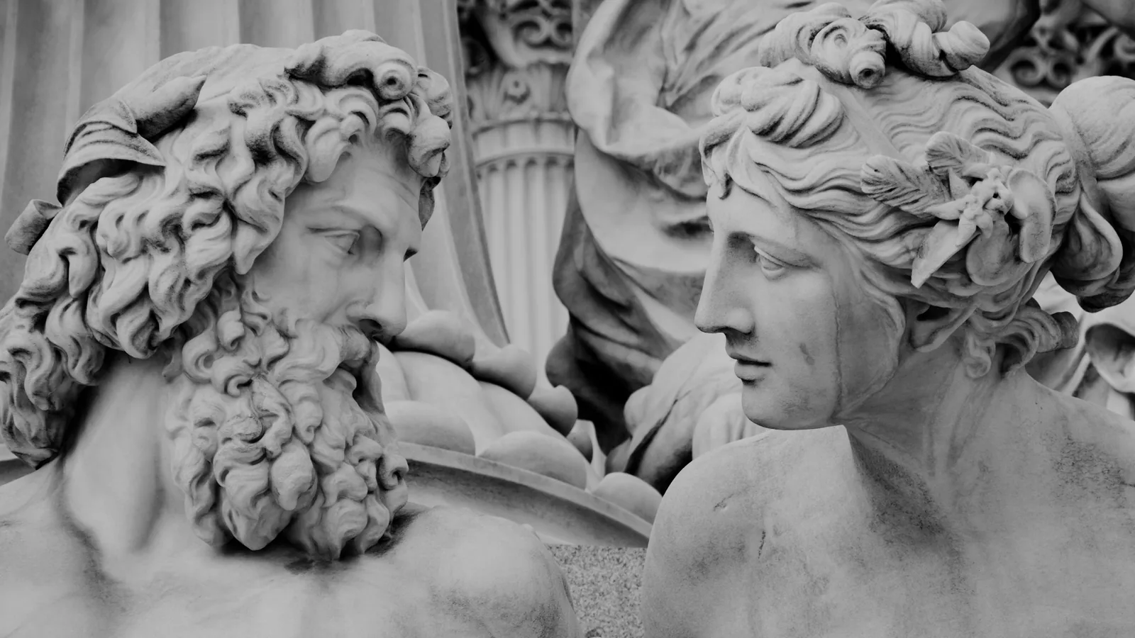 Marble statues of a bearded man and a woman facing each other in classical Greek style