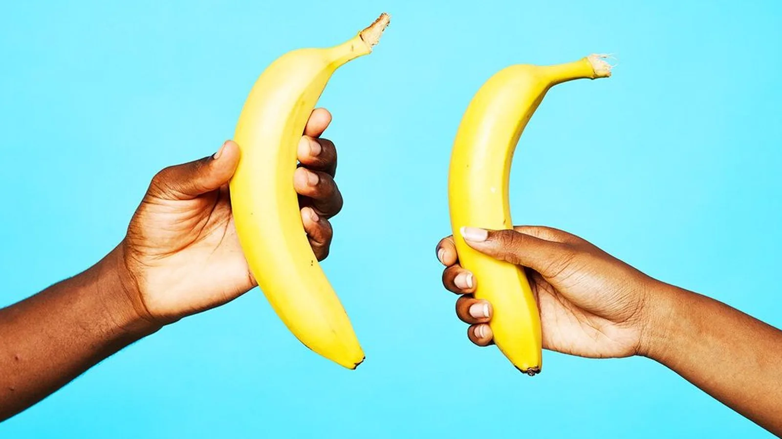 Two hands holding bananas toward each other against a blue background
