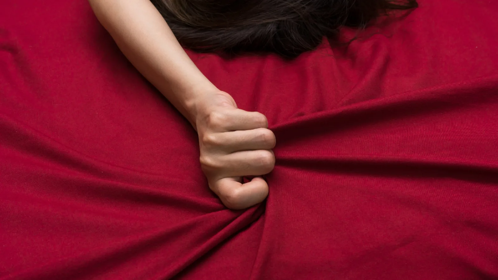 A hand gripping a deep red bedsheet