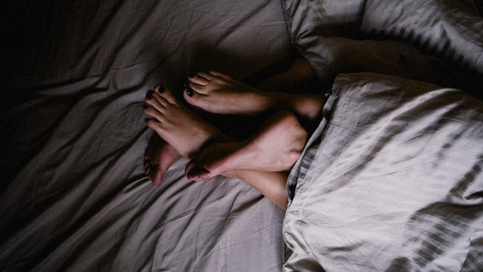 Two pairs of feet intertwined on rumpled gray sheets