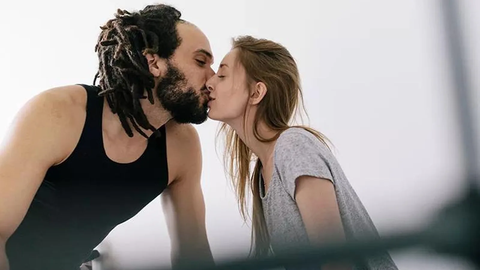 A couple in casual clothes sitting on a bed and kissing in bright daylight